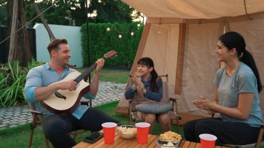 Aile birlikte kamp yapıyor. Anne ve kızı, babasının gitar çalışını dinliyor. Ebeveynler, genç nesil arasında iletişim kurmak ve zaman geçirmek için açık hava kamp faaliyetlerini kullanırlar. Uyumsuzluk.