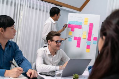 Çeşitli ofis çalışanlarından oluşan bir grup, toplantı odasındaki beyaz tahtaya yapışkan bir notla stratejik iş pazarlama planlaması üzerine beyin fırtınası yapıyor. İş yerinde verimli bir takım çalışması. Tedbirli