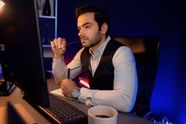 Stresli akıllı işadamı, kağıt işleri üzerine not pazarı verileri yazarak, gece geç saatlerde mor neon karanlık aydınlatma odasındaki disiplin ürünü hizmetlerinin çevrimiçi satış kanalını analiz ediyor. Tahmin et..