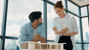 Beyaz mimar mühendis takımı ev modelini ölçmek için birlikte çalışıyor. Genç, güzel tasarımcı ev inşaatı yazarken erkek işçiler mimari modelleri inceliyor, inceliyor, inceliyor. Tartışma