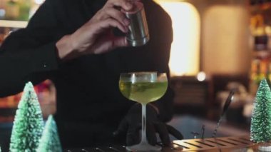 Yakın plan barmen, karamelleştirilmiş turunçgillere tarçın gücü veriyor buz yeşili Midori Sour kokteyli lüks bar ortamlarında lüks Noel temalı çay tabağı içinde servis ediliyor. Vinosity.