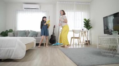 Beyaz anne ve Asyalı çocuk birlikte ev işi yapıyor ve müzik eşliğinde dans ediyorlar. Çekici anne ve kız modern yatak odasını temizlerken şarkı söyleyip rahatlatıcı müziğe atlıyorlar. Yaşam tarzı. Pedagoji.