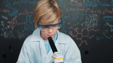 Akıllı çocuk BTMM bilim sınıfında ya da kimya dersinde mikroskop analiz numunesi kullanıyor. Kafkasyalı mutlu öğrenci tüplerdeki kimyasal sıvıyı incelemek için mercek altına bakıyor. Etkinlik.