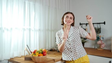 Enerjik beyaz anne kahvaltı için salata pişirirken ve yemek pişirirken elinde kepçeyle şarkı söylüyor. Sağlıklı yemek yapmaya hazırlanırken müziğe yönelen mutlu ev sahibi. Pedagoji.
