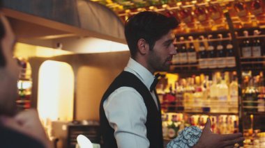 Canlı bir gece partisi atmosferinde lüks bir tezgah barda özel bir içki barında oturan güzel bayan konuğa odaklanıyorum. Müşteriyle konuşurken cam siliyormuş. Vinosity.