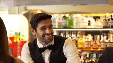 Güzel görünümlü barmen, içki tezgahındaki çiftle samimi bir gülümseme sohbeti yaparken aynı zamanda hoş geldin içkisi ve özel menü listesi öneren çekici profesyonellik. Vinosity.