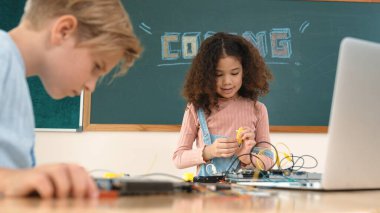 Kız tornavida kullanarak elektronik tahtayı tamir ederken ayakta duruyor. Amerikalı öğrenci ve beyaz çocuk elektrik sistemini denetlemek için birlikte çalışıyorlar. Gemide çalışan meraklı çocuklar. Pedagoji.