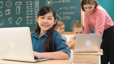 Akıllı Asyalı kız, mühendislik komut yazarken kameraya bakıyor. Çok kültürlü bir öğrenci yapay zekayı öğrenirken öğretmenler sistemi öğretiyor ya da STEM sınıfında sınıfları kontrol ediyor. Pedagoji.