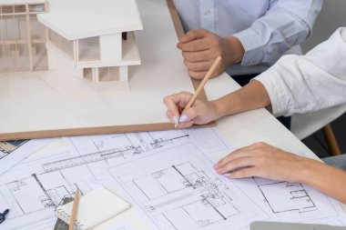 Asyalı kooperatif iş arkadaşı ev modelini ev modeliyle ve bina planıyla birlikte masaya koyarken, profesyonel güzel mimarın el yapımı taslaklarının en üst görüntüsü. Tertemiz..