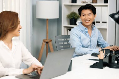 Gülümseyen Asyalı bir adam, yan görüntüdeki modern ofis çalışma masasında veri tabanını ararken günlük dizüstü bilgisayarla pazarlama raporu projesini planlarken kadın meslektaşıyla konuşuyor. İnfobahn.