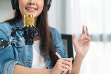 Sosyal medyada kulaklıkla canlı yayın yapan Asyalı sunucu modern stüdyoda yaşam koçluğu veya pazarlama dinleyicilerini selamlıyor. Taktik.