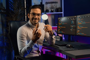 Bilgisayar ekranındaki yazılım geliştirme kodlamasına karşı poz vermek için akıllı bilişim geliştirici görünümlü kamera profilleri, neon ışıklı siber oda ofisinde program güncellemesi internet sitesi verileri sunuyor. Tahmin et..