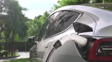 Yavaş çekim EV elektrikli araba yazın yeşil sürdürülebilir şehir parkı bahçesinde şarj oluyor. Elektrikli araç iç organları için kentsel yaşam tarzında sürdürülebilir temiz şarj edilebilir enerji