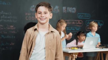 Zeki çocuk kameraya gülümserken çeşitli arkadaşları çalışıyor ya da mühendislik kodlarını öğreniyor ya da BTMM teknoloji sınıfında hızlı çalışıyor. Çocuklar dizüstü bilgisayar kullanırken sevimli bir öğrenci kameranın karşısında duruyor. Etkinlik.