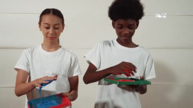 Beyaz kız ve Afrikalı çocuk ellerini suluboya kırmızıya bandırıyor - mavi ya da kontrastlı renge ve sanat dersinde beyaz duvarı damgalamak için geri dönüyorlar. Yaratıcılık aktivite konsepti. Öğretim
