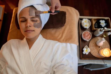 Kaplıca salonunun sakin atmosferi, üst düzey kadın müşteri sıcak mum ışığında kömür kömürü yüz kremi masajıyla kendini yenilemeye çalışıyor. Yüz bakımı ve güzellik konsepti. Sessiz.