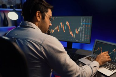Akıllı tüccar işadamı, karanlık oda gecesinde neon ışıklı ofisteki arama pazarında yüksek kârla ekranda bilgisayar ve bilgisayar üzerinde dinamik borsa yatırımları üzerinde yoğunlaşıyor. Tahmin et..