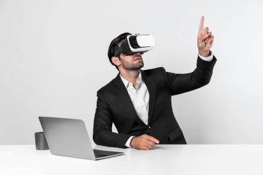 Bilgisayarla masada otururken ve VR gözlüğü takarken veri analizine bakan yetenekli bir iş adamı. Proje yöneticisi sanal gerçeklik sistemini kullanarak ya da metaevrende bağlantı kurarak çalışıyor. Sapma.