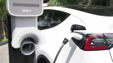 Yavaş çekim EV elektrikli araba yazın yeşil sürdürülebilir şehir parkı bahçesinde şarj oluyor. Elektrikli araç iç organları için kentsel yaşam tarzında sürdürülebilir temiz şarj edilebilir enerji