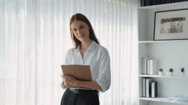 Klinikteki dost canlısı psikolog kadın. Profesyonel portresi. Kameraya bakıp psikolog muayenehanesine bakıyor. Tecrübeli ve kendinden emin psikolog.