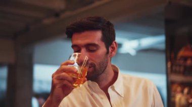 Profilde, beyaz tişörtlü, gülümseyen zeki bir adamın cuma gecesi lüks bir barda özel parti içeceği kokteylinden kokteyl içtiği görülüyor. Vinosity.