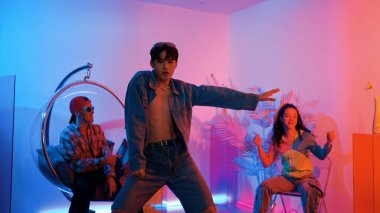 Çok kültürlü bir arkadaş kürsüde otururken Asyalı yetenekli bir dansçı modern müziğe geçiyor. Profesyonel dansçı, hipster takımı tezahürat yaparken ve desteklerken enerjik adımlar atıyor. Mutluluk.