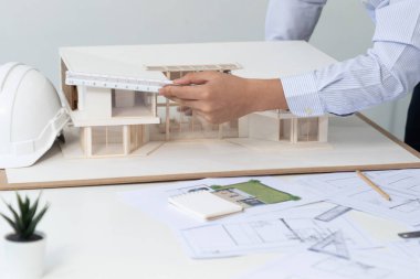 Asyalı kooperatif iş arkadaşı ev modelini ev modeliyle ve bina planıyla birlikte masaya koyarken, profesyonel güzel mimarın el yapımı taslaklarının en üst görüntüsü. Tertemiz..