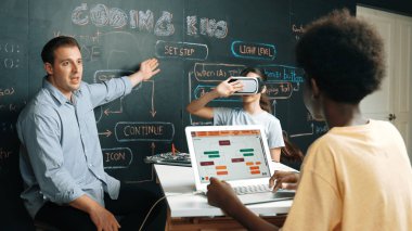 Akıl hocası karatahtayı işaret ederken ve mühendislik kodunu açıklarken VR gözlüğü takıyor. Afrikalı öğrenci yazma sistemi, öğretmenden elektronik aletlerle tavsiye alırken. Öğretim.