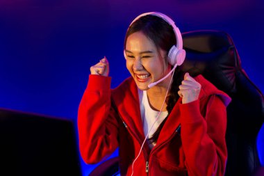 Yüzünde kulaklık renginde kulaklık takan, neon odada online oyun oynayan, Esport meziyetli takım oyuncularına yumruk kaldırarak oynayan güzel Asyalı kız flamasının sunucu kanalı. Taktik.