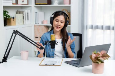 Sosyal medyada kulaklıkla canlı yayın yapan Asyalı sunucu modern stüdyoda yaşam koçluğu veya pazarlama dinleyicilerini selamlıyor. Taktik.