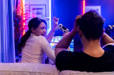 Gülümseyen güzel kadın oyuncu, arka taraftaki zavallı adamın yanında video oyununda dövüşüyor. Televizyondaki bir kaç oyuncu stüdyo odasındaki kırmızı mavi ışıkta joystick kullanıyor. Varsayım.