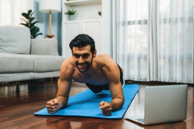 Atletik ve sporcu adam, evdeki formda fiziğe ve sağlıklı spor yaşam tarzına uygun vücut egzersizi sırasında spor minderinde kalas yapıyor. Gaiety evde egzersiz eğitimi.