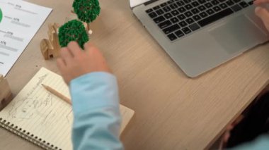 Temiz enerji ve ahşap blokla temsil edilen yel değirmeni modeli ekoloji evini sembolize ediyor. İş adamı dizüstü bilgisayar ve dizüstü bilgisayar üzerinde çalışıyor ve masadaki gelecek binaları tasarlayıp hesaplıyor. Tanımlama.