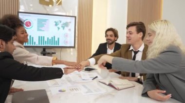 Çeşitli ofis çalışanları, işyerindeki iş sinerjisini ve üretken takım çalışmasını sembolize eden süslü ofis odasında el ele tutuşuyorlar. İş çalışanları arasındaki işbirliği ve birlik.