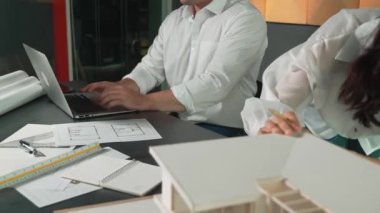 Bir grup mimar mühendis birlikte çalışıyor ve ofis tasarımı hakkında tartışıyorlar. Genç mühendis ev modelini ölçerken yönetici dizüstü bilgisayar kullanıyor. İş tasarımı konsepti. Yönlendirici.