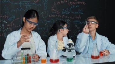 Akıllı genç kız kimya teorisi ile tahtayı dikkatlice incelerken mikroskop altında numune bırakıyor. Profesyonel bilim adamı tüpün içine kimyasal madde döker ve deney için hazırlanır. Öğretim