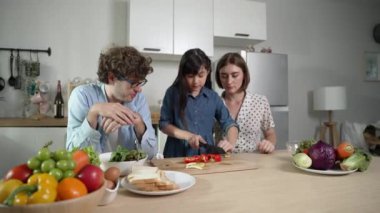 Çekici beyaz anne ve baba Asyalı kızıyla taze yemek pişirmek için birlikte vakit geçiriyorlar. Enerjik anne ve baba mutfakta salata yapmak için taze sebze hazırlıyor. Sağlıklı yiyecekler. Pedagoji.