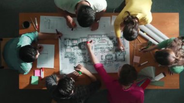 İnşaat mühendisi ekibinin renkli paletlerle toplantı masasında yazı yazması. Yönetici proje planlarına bakarken bir grup farklı insan plan yapıyor ve not alıyor. Sempozyum.