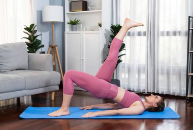 Spor kıyafetleri içinde esnek ve becerikli bir kadın evde egzersiz paspası üzerinde meditasyon pozisyonunda yoga yapıyor. Huzurlu ve huzurlu bir yoga yaşam tarzı..