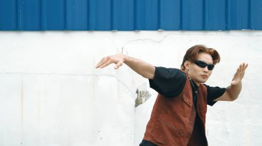 Beyaz arka planda break dans pratiği yapan yakışıklı bir sokak dansçısı. Hip hop tarzı giyinen sporcu, mavi arka planlı bir sokakta müzik eşliğinde ayak sesleri çıkarıyor. Açık hava sporu 2024 hiphop..