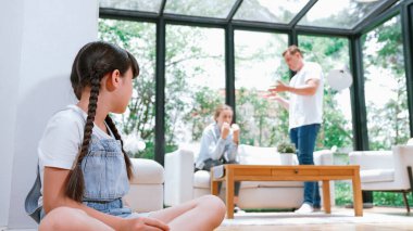 Stresli ve mutsuz genç kız köşeye kıvrılıp kulaklarını kapatarak arka planda ebeveyninin tartışmasını engelliyor. Evde aile içi şiddet ve travmatik çocukluk depresyona dönüşür. Eşzamanlama