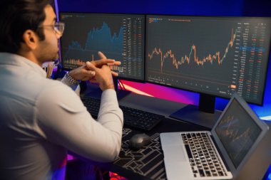 Akıllı tüccar işadamı, karanlık oda gecesinde neon ışıklı ofisteki arama pazarında yüksek kârla ekranda bilgisayar ve bilgisayar üzerinde dinamik borsa yatırımları üzerinde yoğunlaşıyor. Tahmin et..