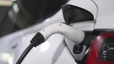 Yavaş çekim yakın EV elektrikli araba şarj istasyonunda fişe takılı, şehir merkezindeki alışveriş merkezinin otoparkında şarj bataryasını şarj ediyor. Elektrikli araç iç organları için temiz yeşil sürdürülebilir enerjisi var.