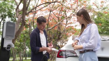 Yavaş çekim genç çift sonbaharda ulusal parktaki EV şarj istasyonunda EV elektrikli arabaları şarj ediyor. Tatil ve sonbahar sezonunda çevre dostu arabalarla seyahat. Yararlı