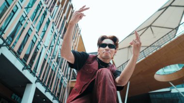 Asyalı çekici hipsterin düşük açılı pozu alışveriş merkezinin etrafını sarmış durumda. Break dans koreografının portresi hip hop tarzında dans ederken kameraya bakıyor. Açık hava sporu 2024. Hiphop.