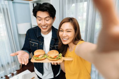 Gülümseyen sunucu şefler akıllı telefonlarıyla fotoğraf çekiyorlar. Özçekim yoluyla. Yemek programında çift hamburger tutuyorlar. İnfobahn.