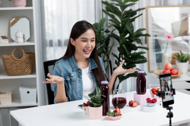 Gülümseyen, güzel Asyalı genç, lezzetli karışık çilek ve kiraz suyu detoksu içeceklerini inceleyen, sosyal medyada özel promosyon satışı için sağlıklı ürünler sergileyen. Taktik.