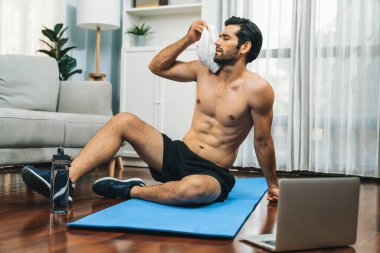 Sporcu ve atletik bir adam evde vücut egzersizlerini bitirdikten sonra spor minderinde dinleniyor. Formda ve sağlıklı bir yaşam tarzı için. Gaiety evde egzersiz eğitimi.