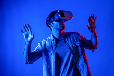 Sanal programı keşfetmek ve girmek için VR gözlük takan heyecanlı bir adam. Yetenekli oyuncular metaevrene dokunurken gündelik giysiler giyer ve neon ışıklı arka planda dururlar. Yaşam tarzı. Sapma.