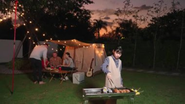 Aile hep birlikte bahçede kamp kurar, tatlı kız ızgara yapar aile ferdi için. Doğayla iç içe olmak ve ebeveynlerle ya da son sınıfların çapraz kuşaklarıyla zaman geçirmek için açık hava kamp aktiviteleri. Uyumsuzluk.